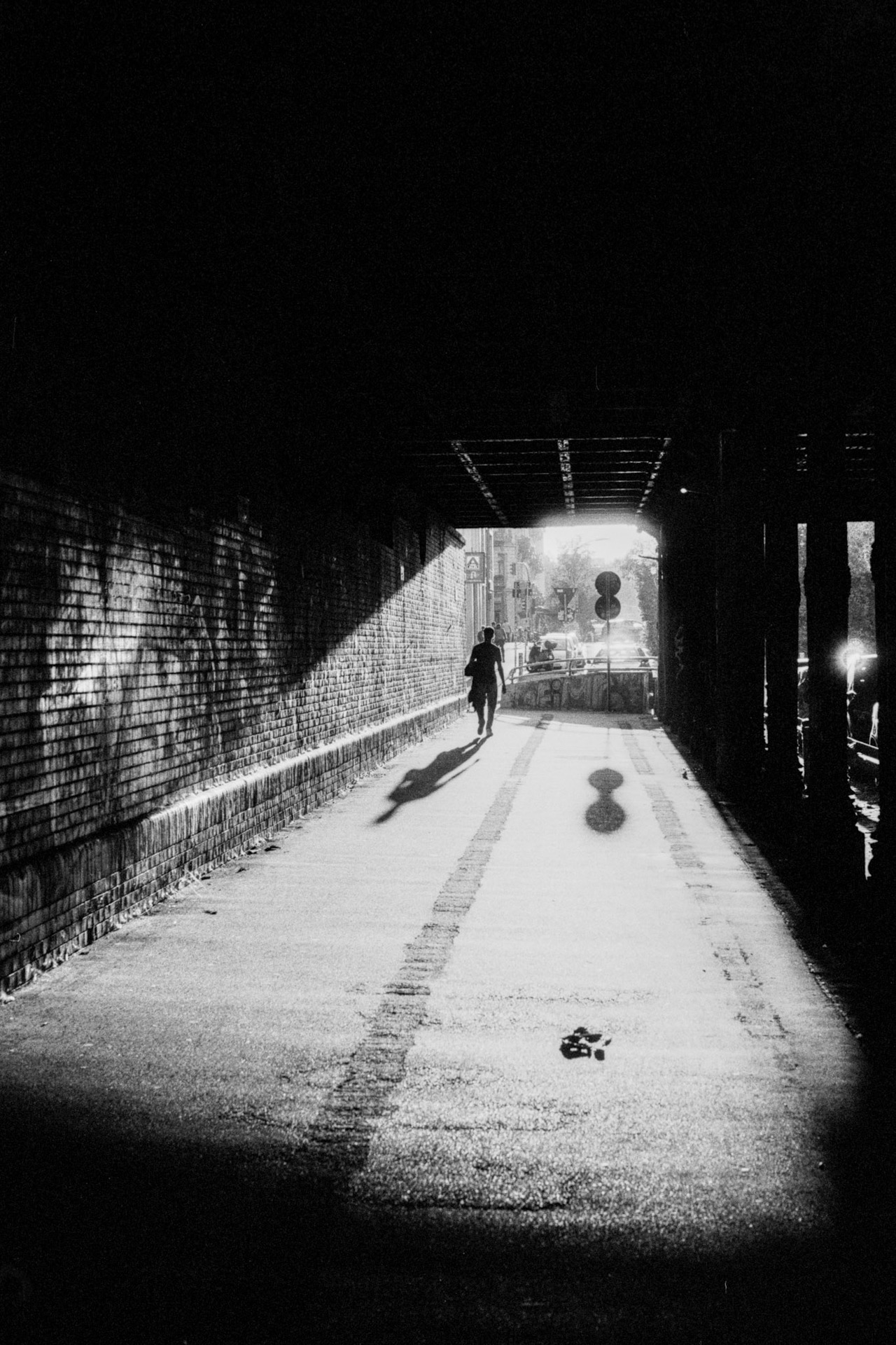 A person walking through a railway underpass toward the light, a graffiti-covered brick wall on the left.