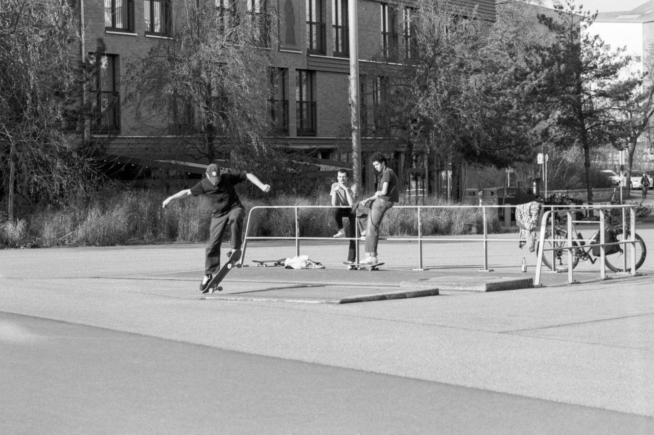 A skateboarder landing a trick on a paved square while two friends watch from a railing.