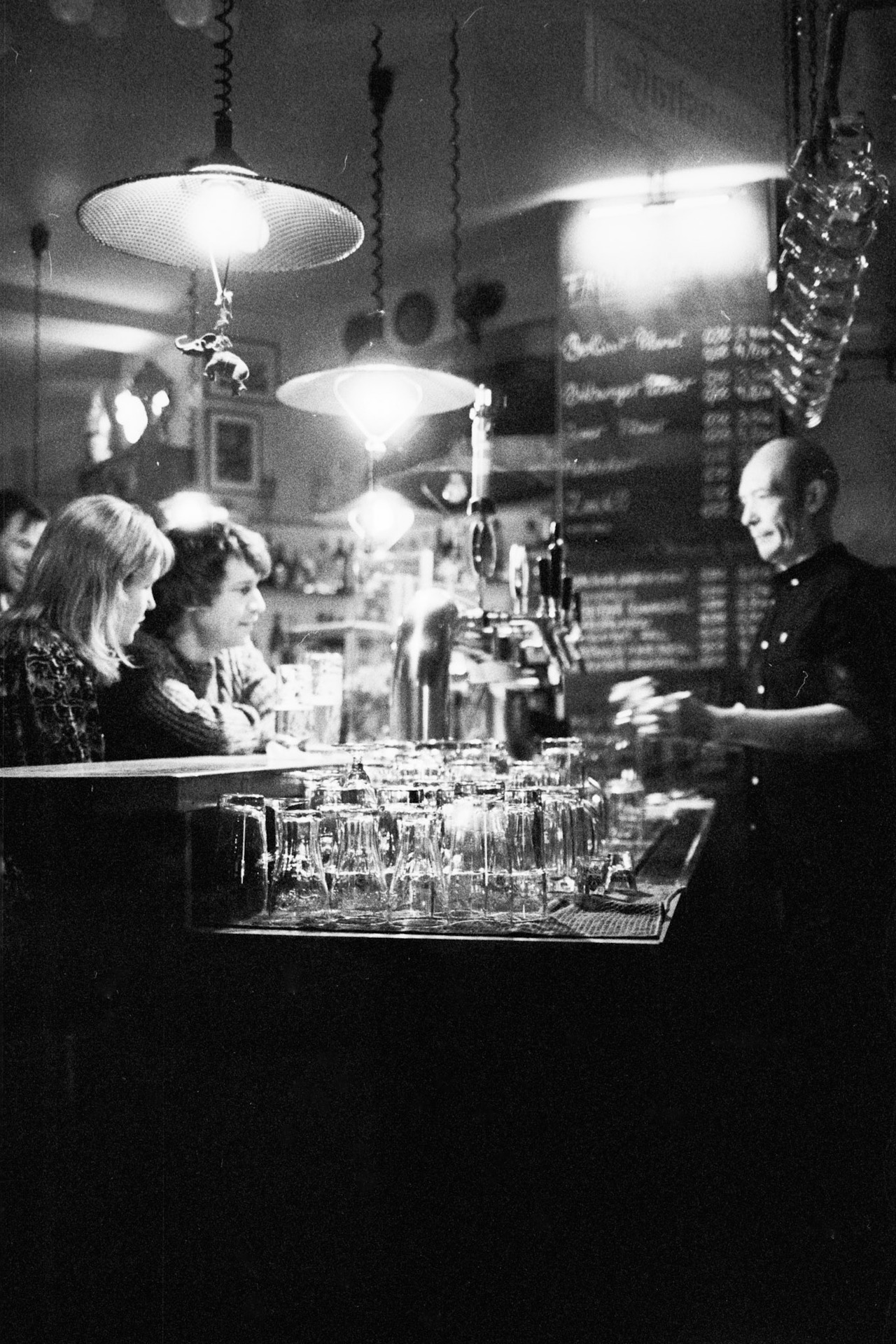 A bartender talking to two women across a counter lined with glasses.