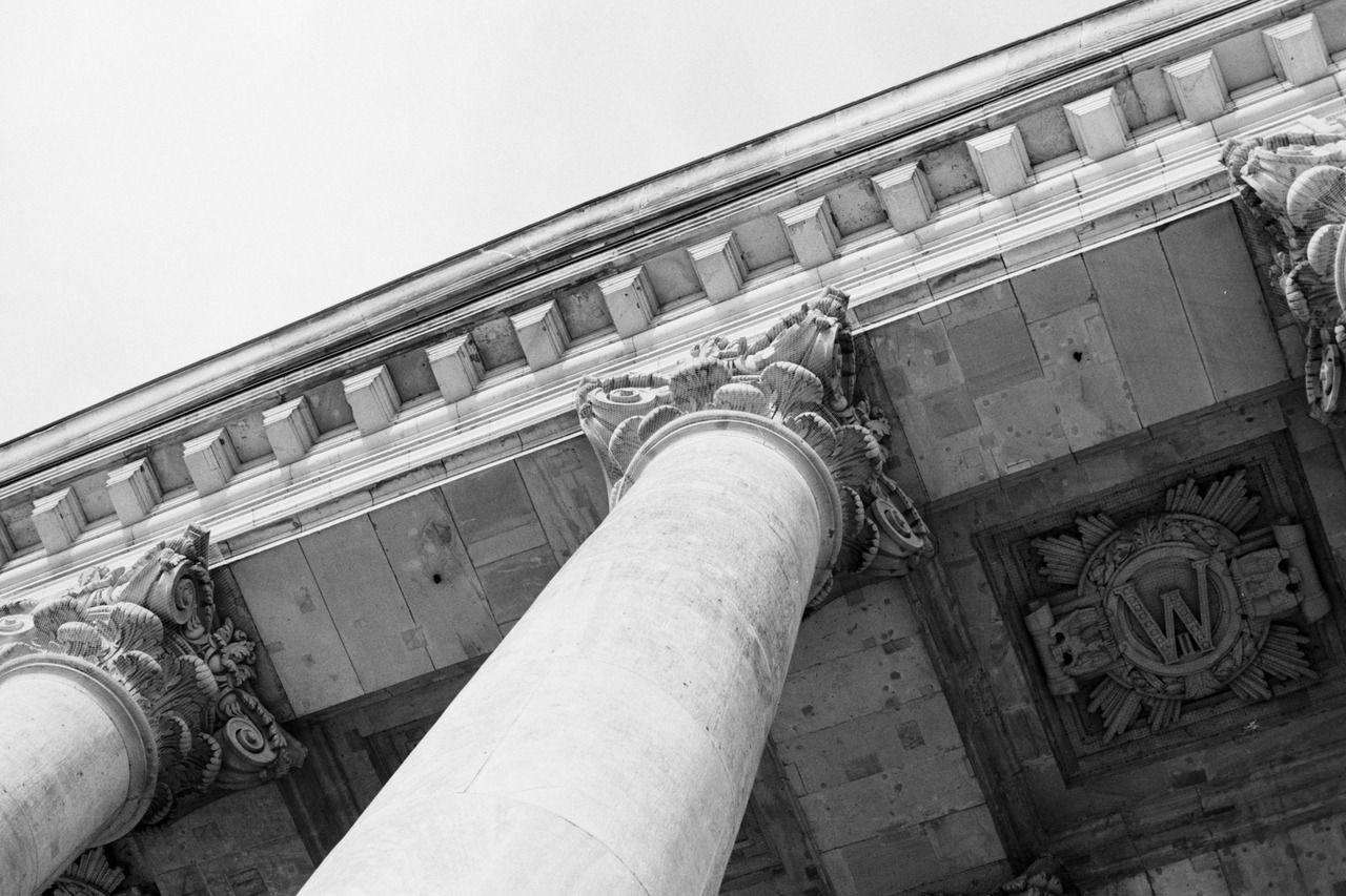 Corinthian columns and a carved emblem seen from below against the sky.