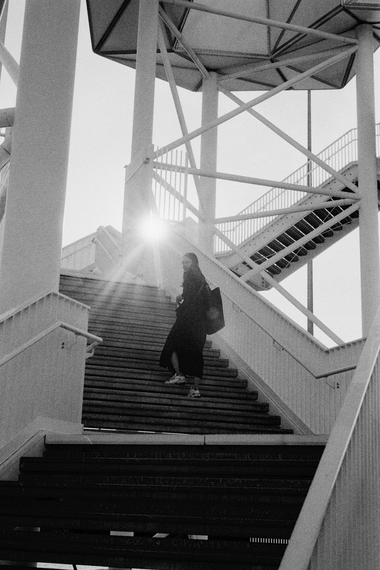 A woman on the stairs of a white steel tower, the sun flaring behind the structure.