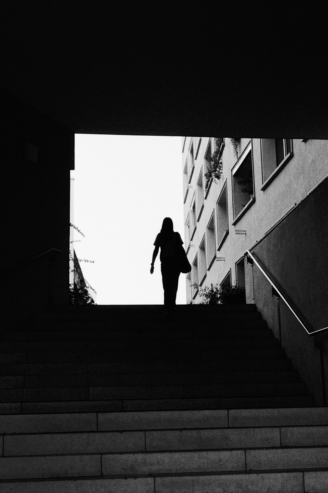 A silhouetted woman climbing stairs from a dark passage toward bright daylight.