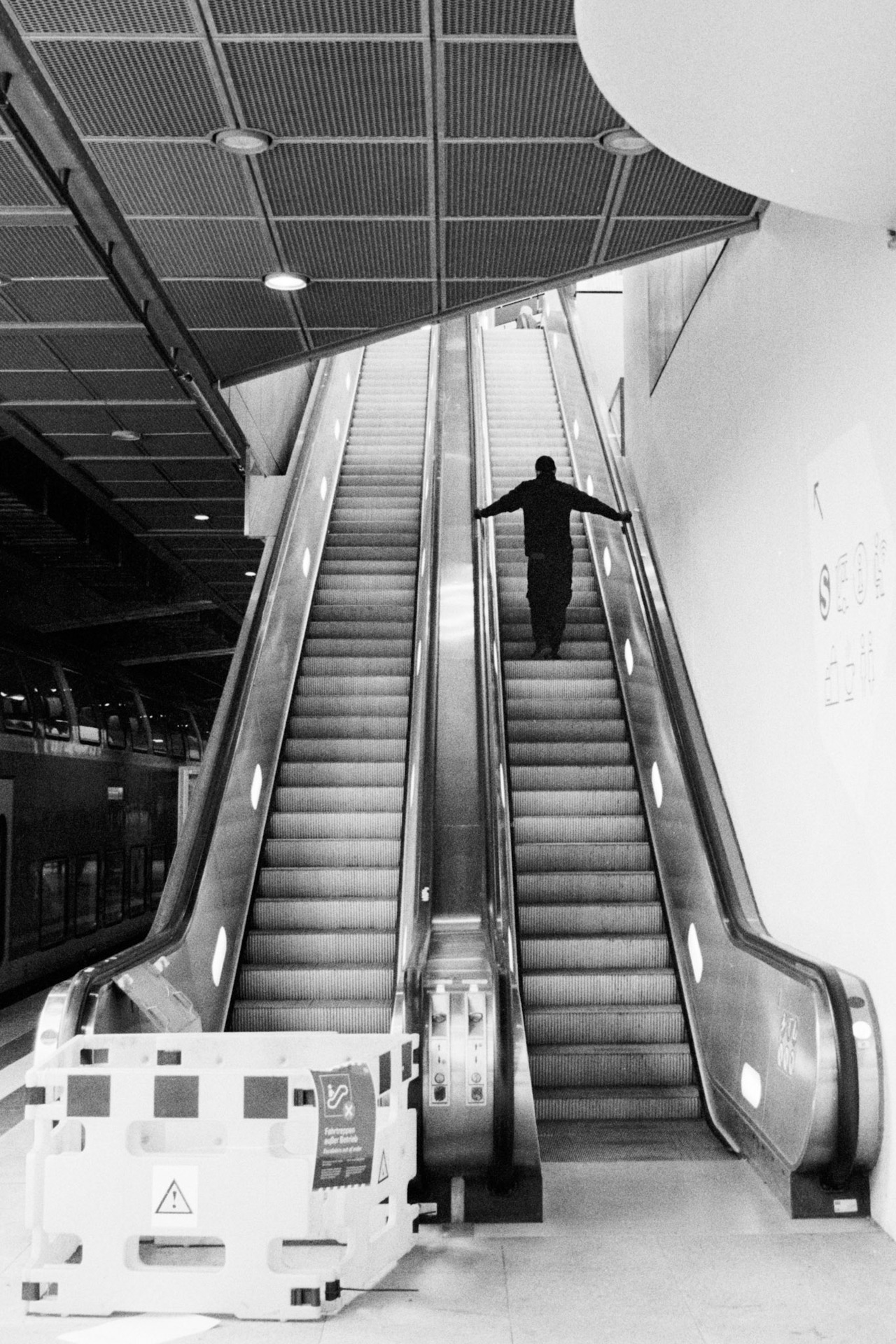 A man with arms outstretched riding an escalator, seen from below.