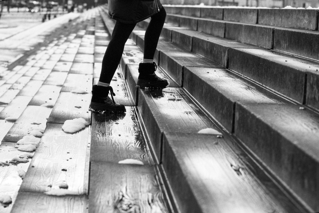 Legs in black boots climbing wet steps scattered with snow.
