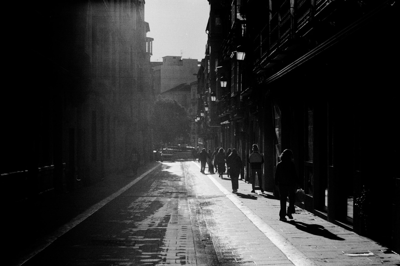 People walking down a narrow street between tall buildings, backlit by the sun.