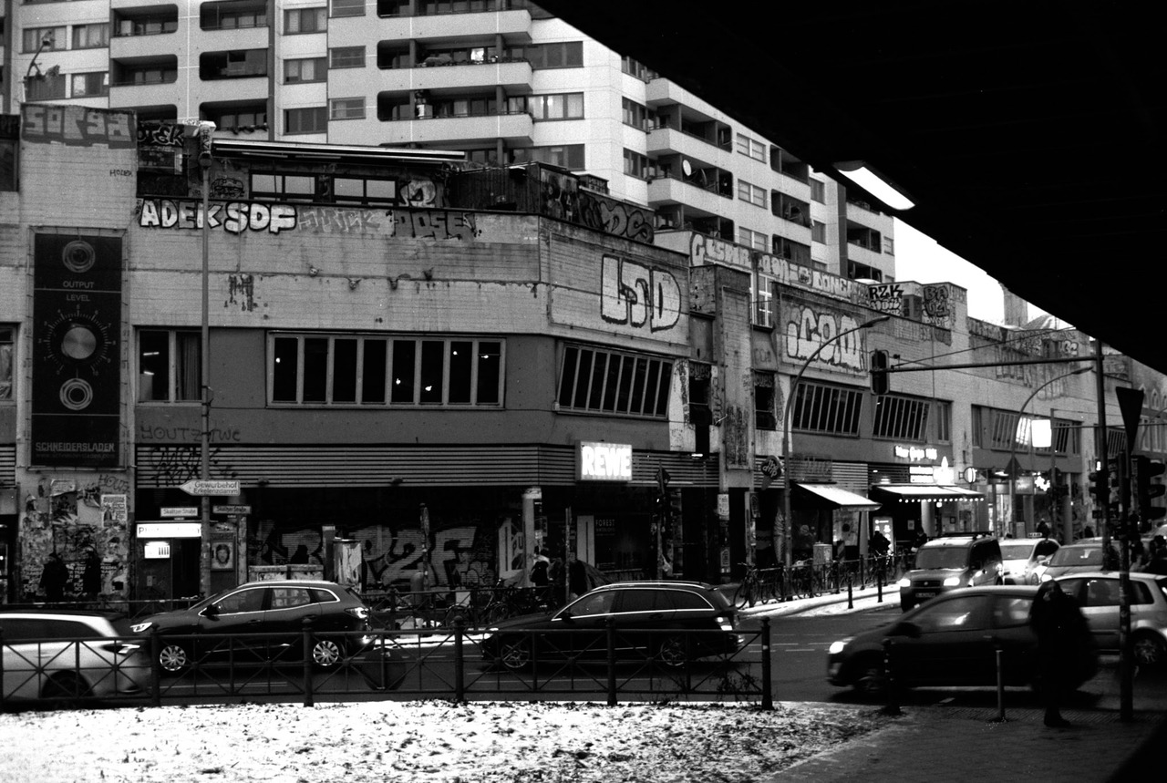 Graffiti-covered buildings and a supermarket sign above a busy junction, cars passing.