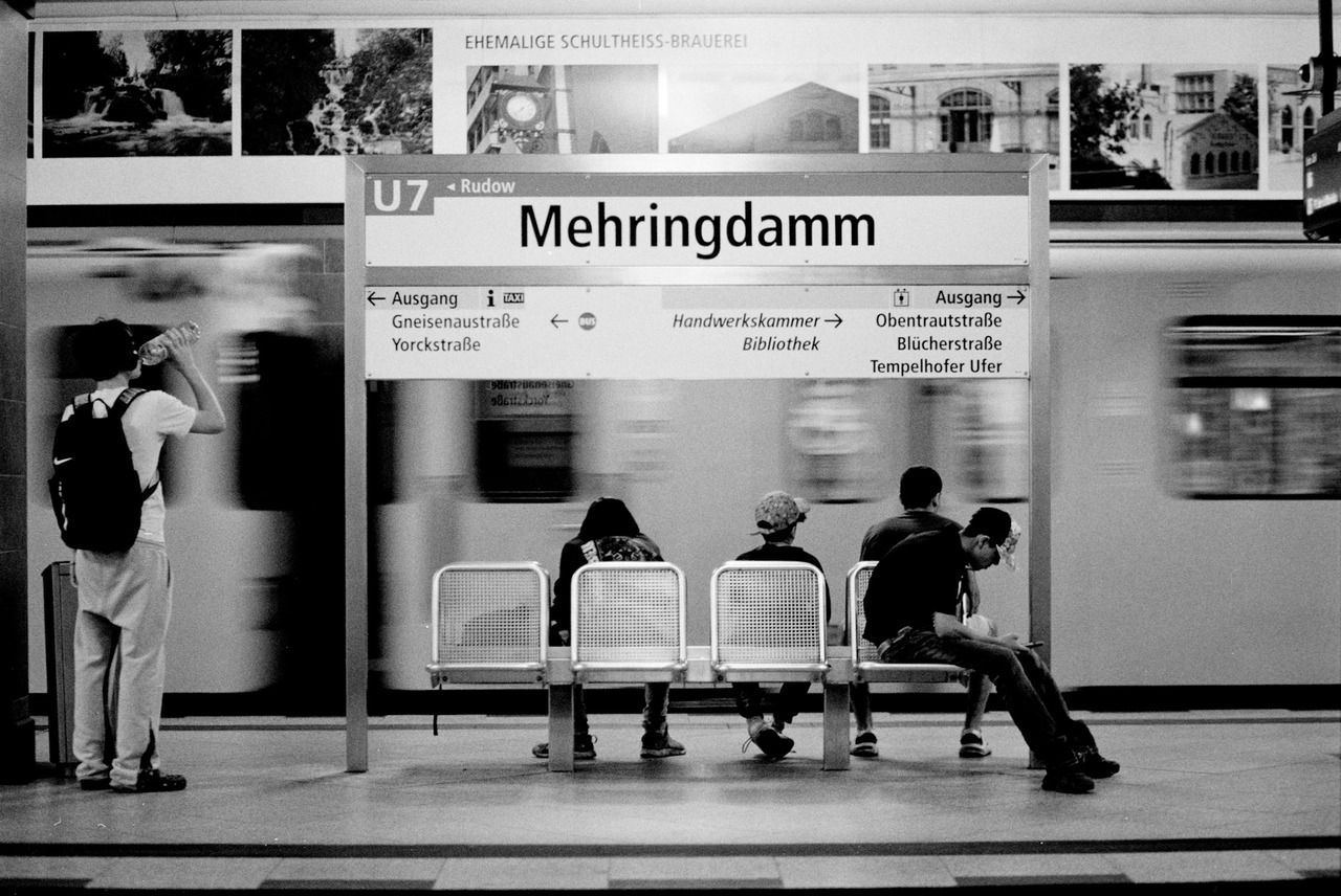 People waiting on seats at Mehringdamm U-Bahn station as a train passes in a blur.