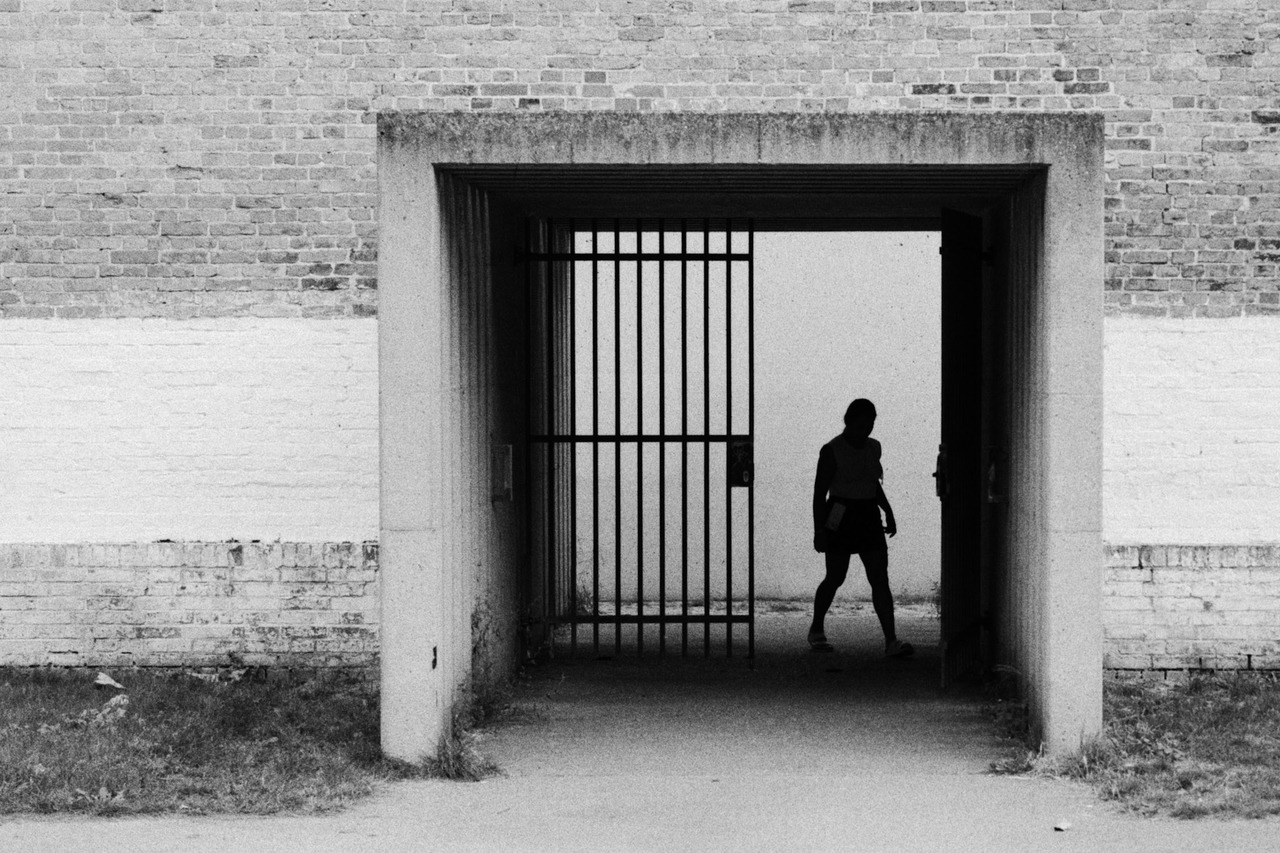 A silhouetted person walking past an open metal gate set in a brick wall.