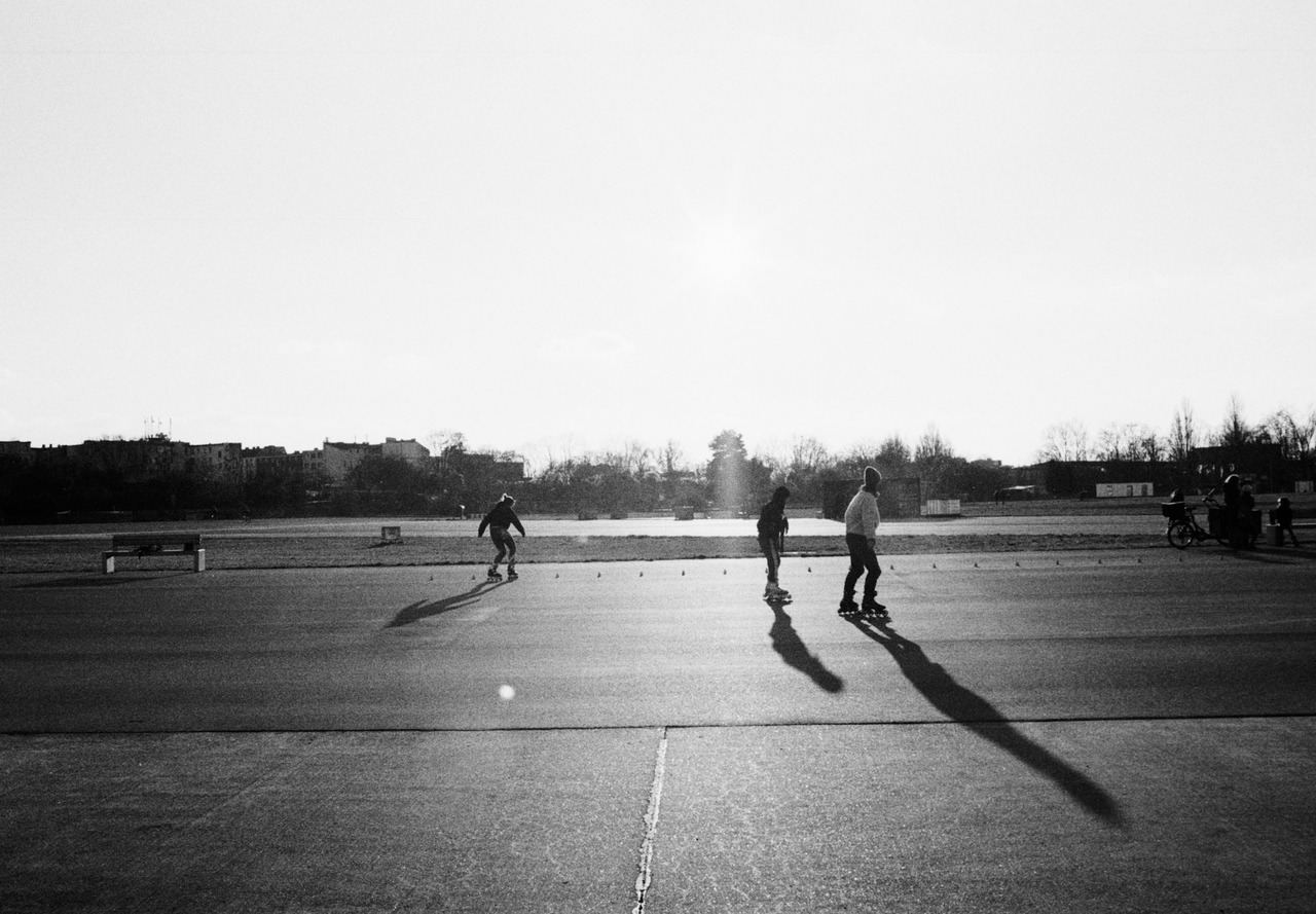 Three inline skaters on an open tarmac field, casting long shadows toward the camera.