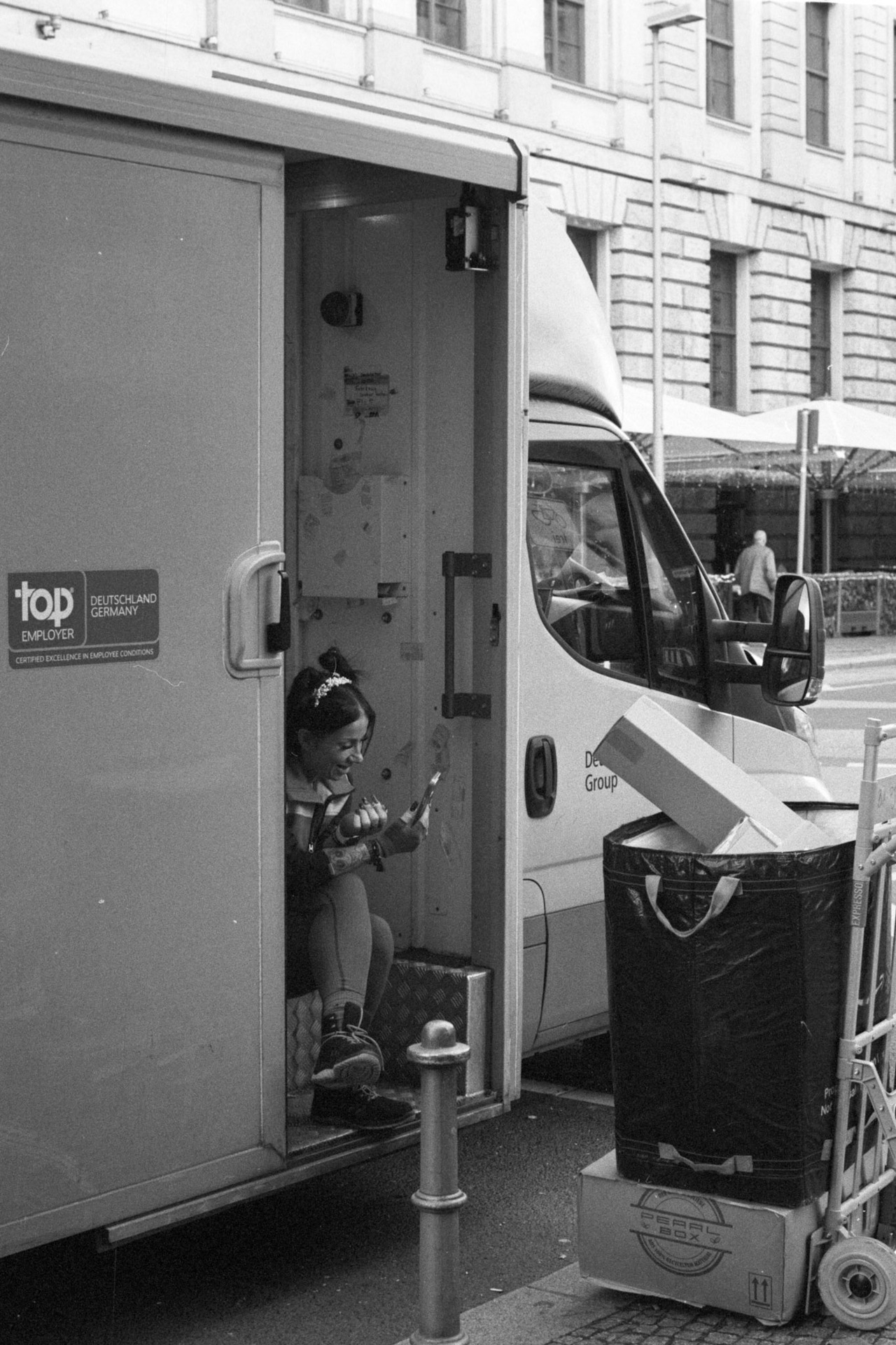 A woman sitting in the side door of a delivery van, looking at her phone.