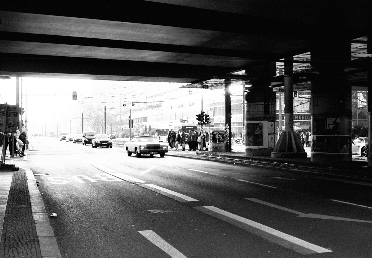 Cars driving out of a sunlit road underpass, a white vintage car in front.