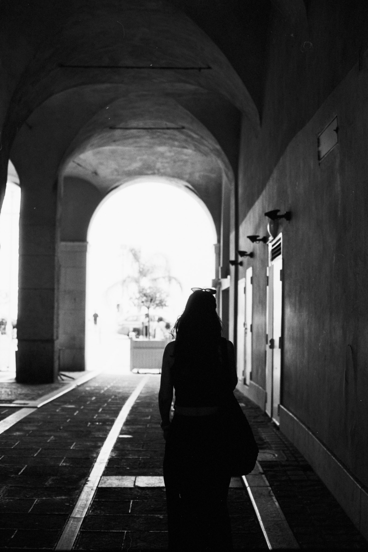 A woman walking toward the bright end of a vaulted passage, silhouetted.