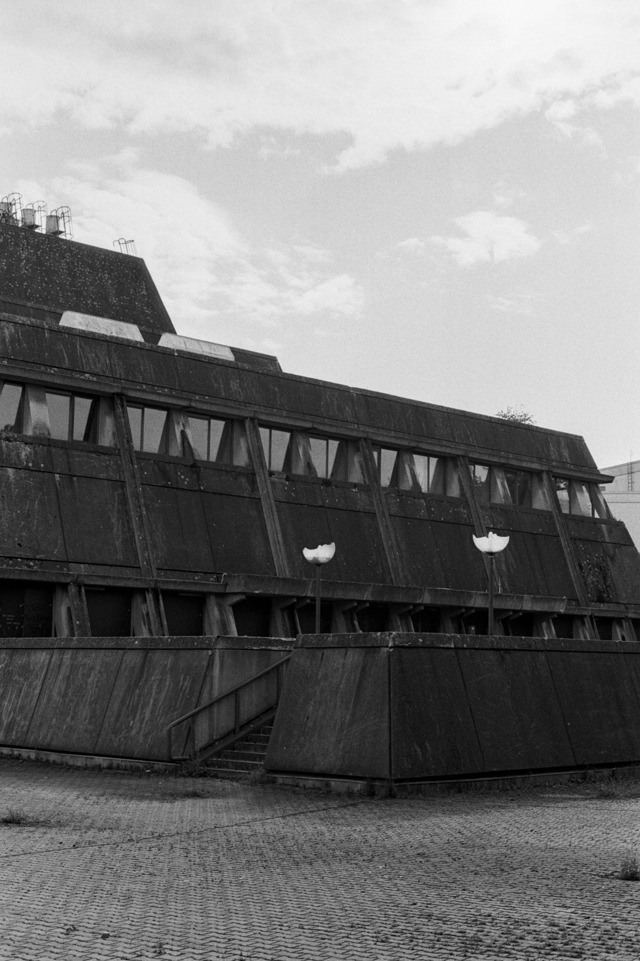 A brutalist building with sloping concrete walls and a flight of steps, under clouds.