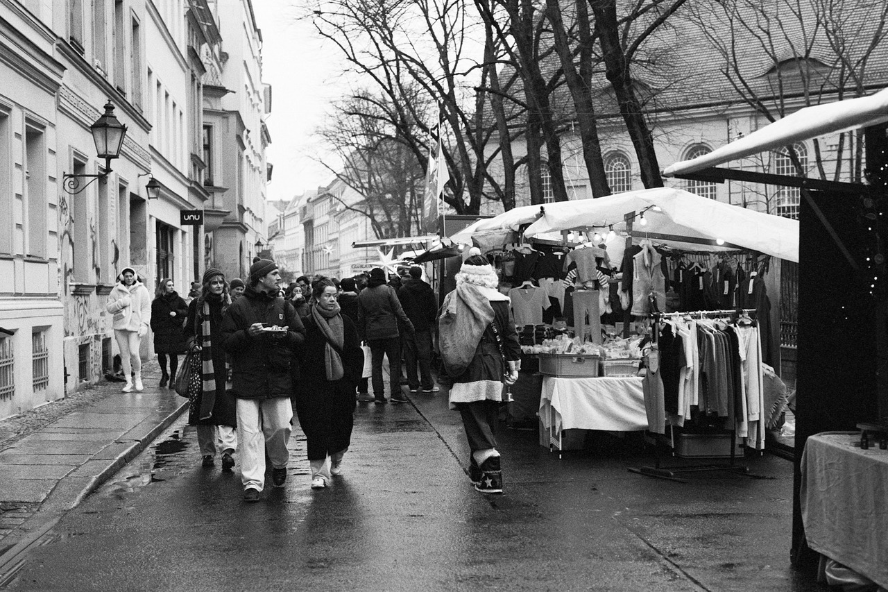 People walking along a wet winter street past market stalls hung with clothes.