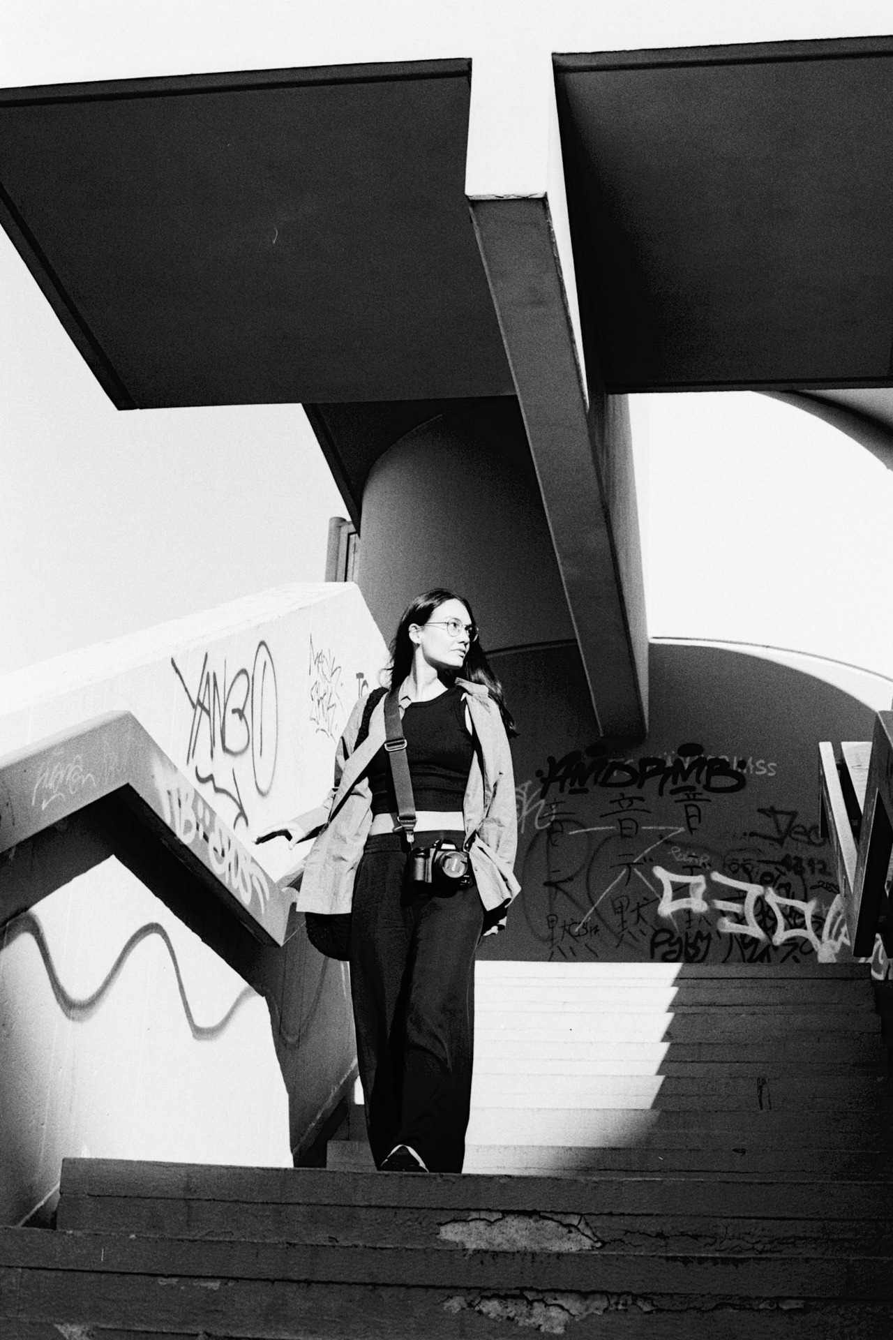 A woman with a camera walking down concrete stairs past graffiti, under a flat overhang.