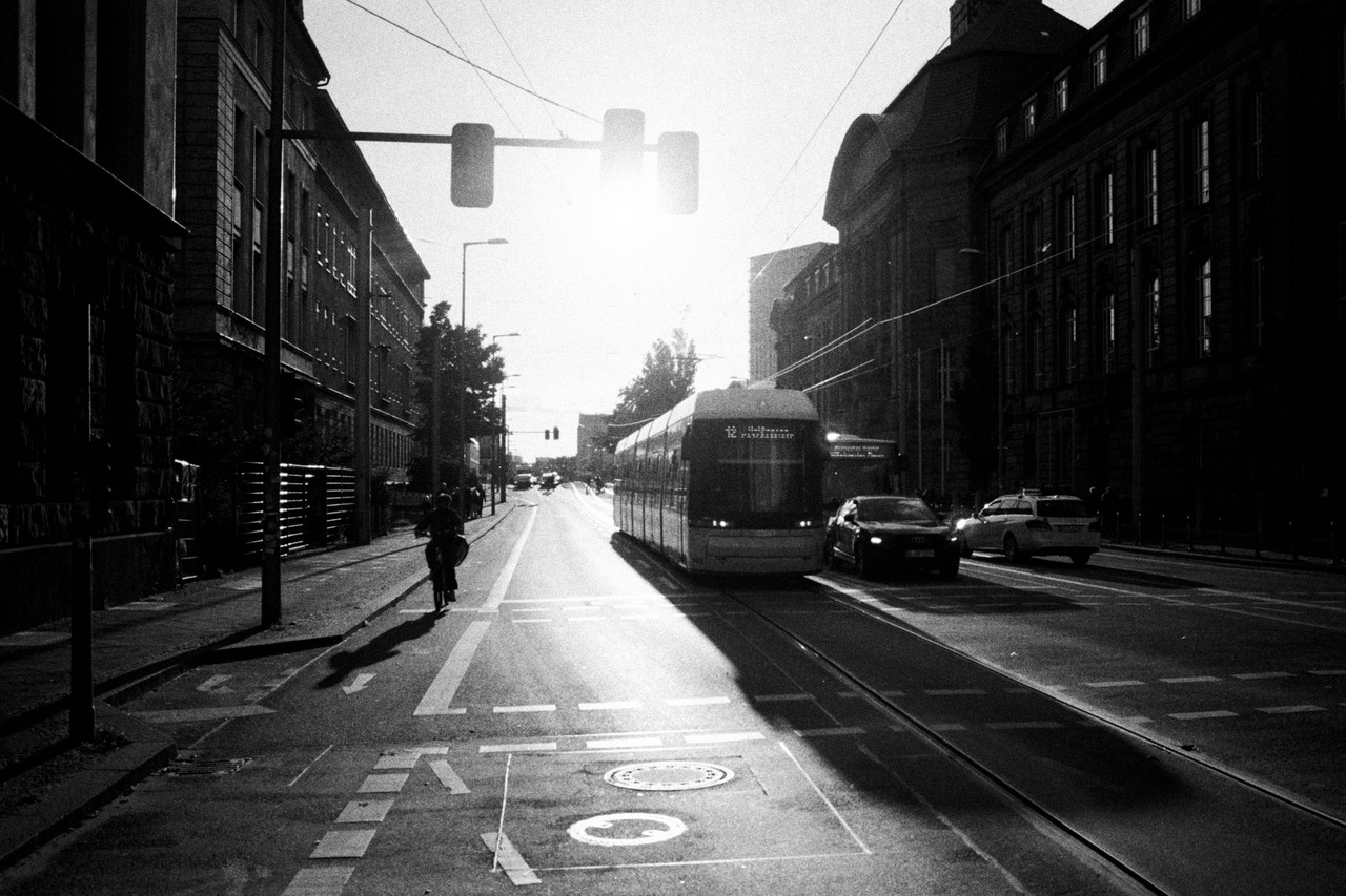 A tram approaching down a wide street into the low sun, a cyclist on the left.