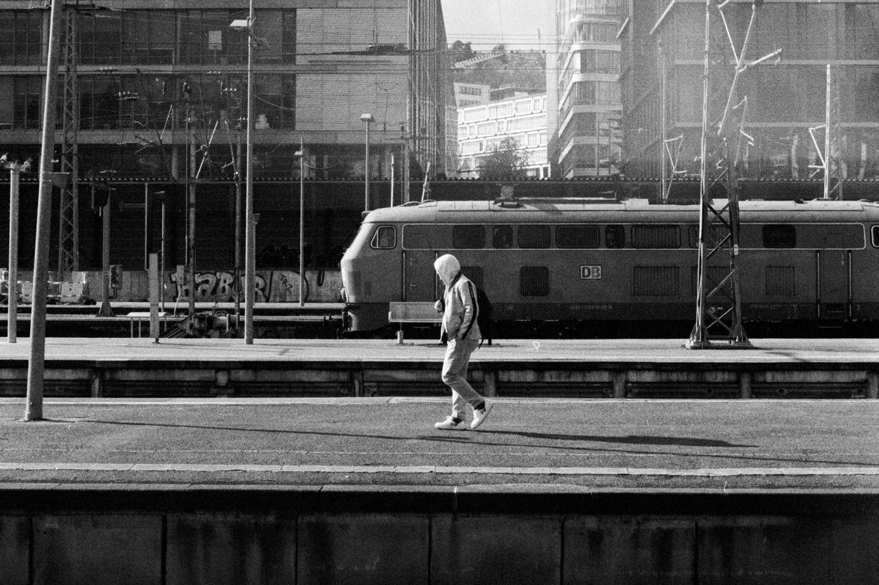 A man in a hooded top walking along a railway platform, a locomotive on the next track.
