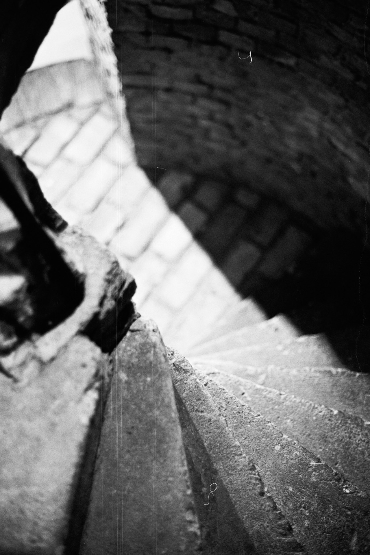 Worn stone steps of a narrow spiral staircase winding around a brick wall.